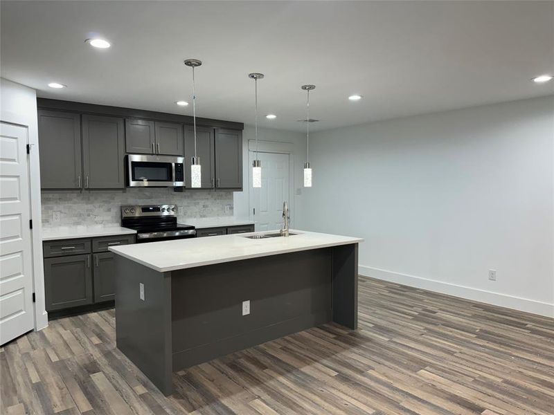 Kitchen with dark wood-type flooring, appliances with stainless steel finishes, hanging light fixtures, and sink