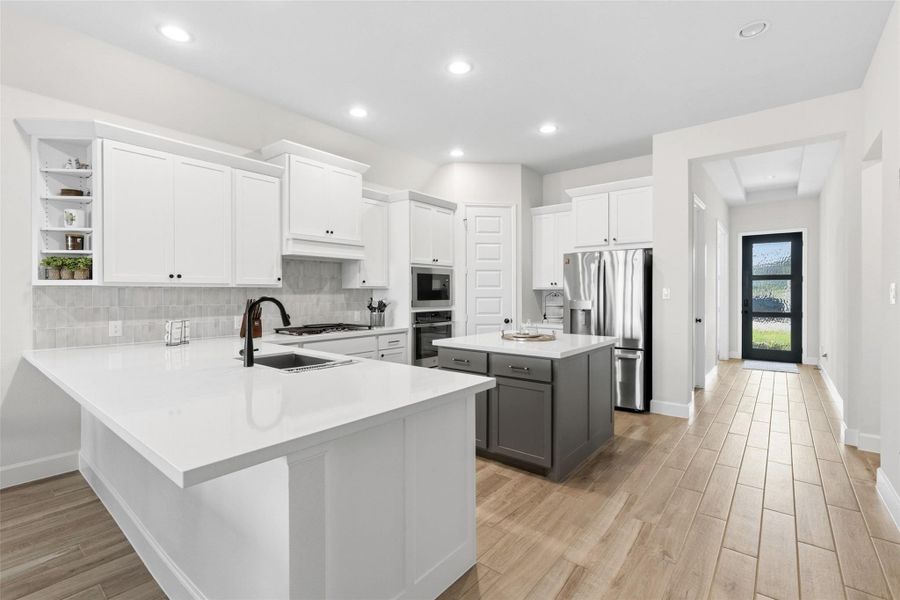 Open-concept kitchen featuring white shaker cabinetry, an expansive central island with a sink and matte black faucet, and a contrasting gray island