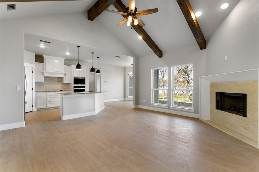 Unfurnished living room featuring beamed ceiling, high vaulted ceiling, ceiling fan with notable chandelier, and light wood-type flooring