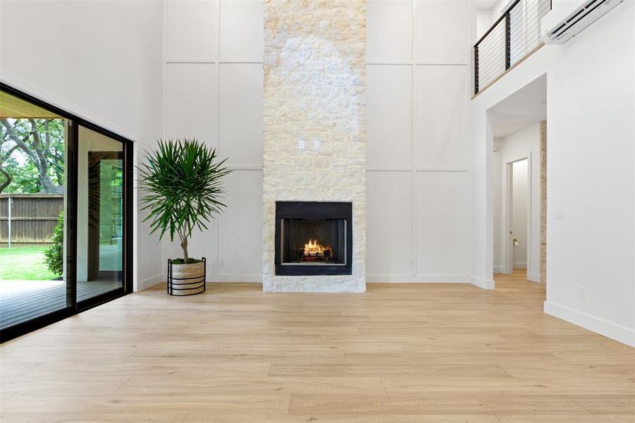 Unfurnished living room featuring a wall mounted air conditioner, light wood-style floors, a towering ceiling, and a stone fireplace