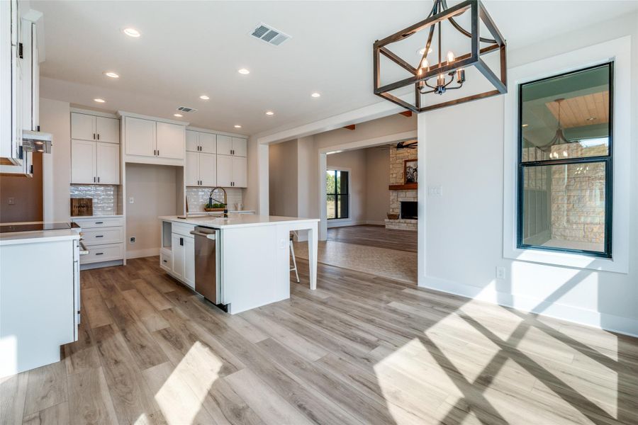 Kitchen with white cabinets, a fireplace, light wood-type flooring, a center island with sink, and a kitchen breakfast bar