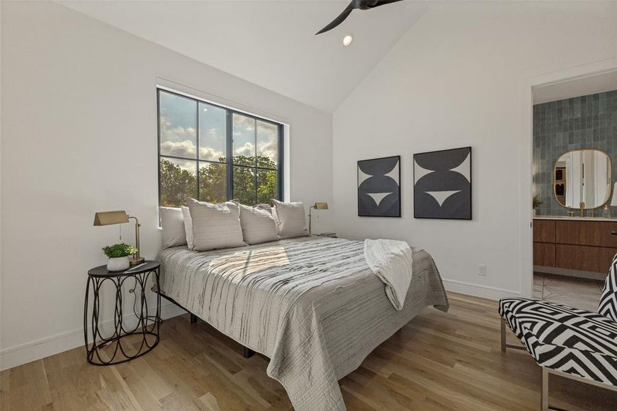 Spacious bedroom featuring vaulted ceilings, wide plank wood-finish flooring, and a large black-framed window Spacious bedroom featuring vaulted ceilings, wide plank wood-finish flooring, and a large black-framed window