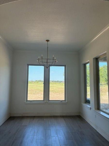 Unfurnished dining area with crown molding, dark wood finished floors, plenty of natural light, and a chandelier