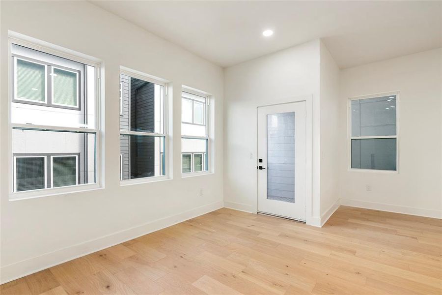 This is a bright, modern room featuring large windows for ample natural light, clean lines, fresh white walls, and light hardwood floors. It includes a contemporary glass door leading to private balcony.