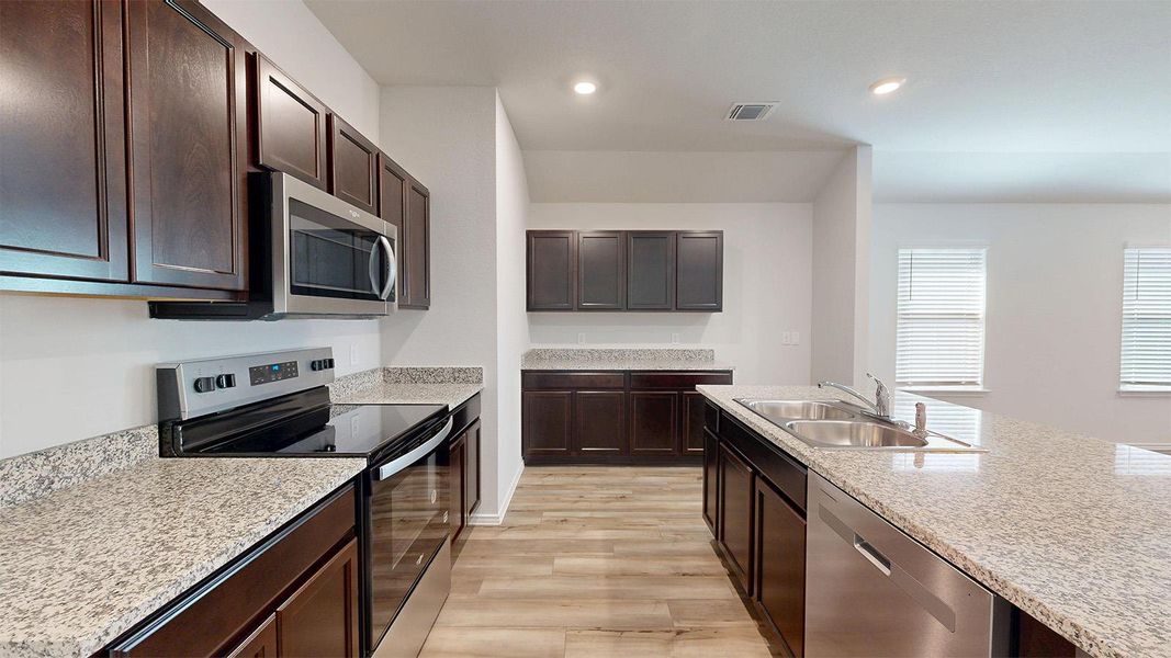 Kitchen with stainless steel appliances, dark wood finish cabinetry, light wood-style flooring, light stone counters, and recessed lighting