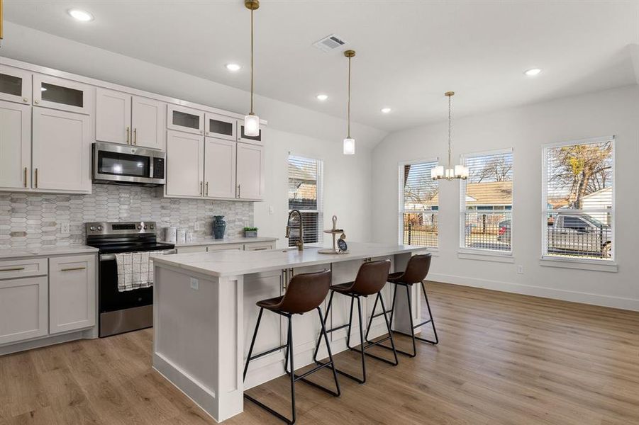 Kitchen with pendant lighting, sink, appliances with stainless steel finishes, white cabinets, and a center island with sink