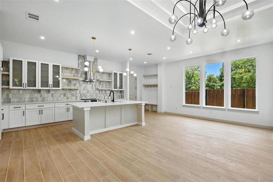 Kitchen featuring a chandelier, open shelves, decorative backsplash, light countertops, and light wood-type flooring Kitchen featuring a chandelier, open shelves, decorative backsplash, light countertops, and light wood-type flooring