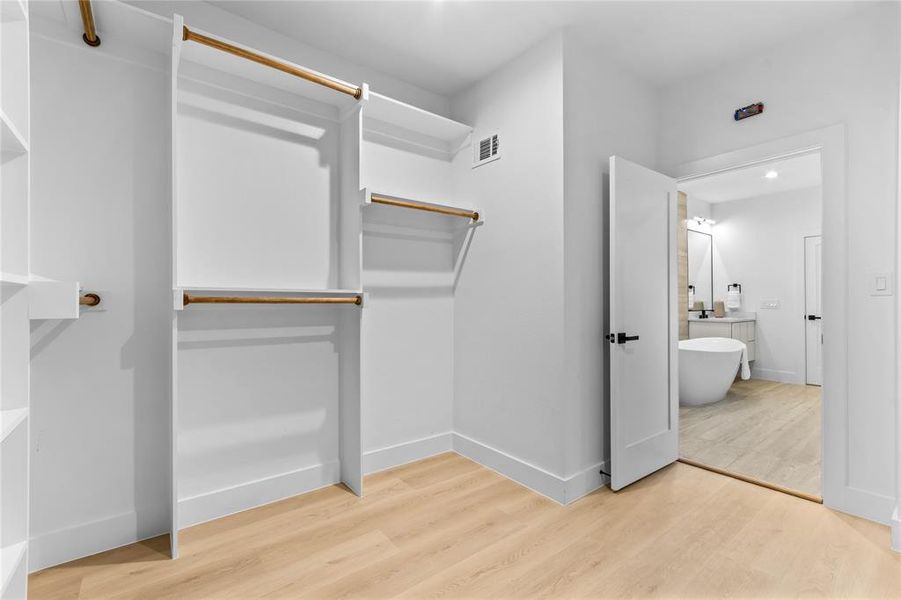 Walk-in closet featuring white built-in shelving, hanging rods, and light wood-finish flooring Walk-in closet featuring white built-in shelving, hanging rods, and light wood-finish flooring