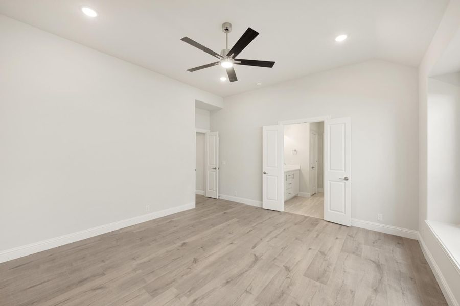 Empty bedroom with light wood floors, ceiling fan, and open door to ensuite bathroom