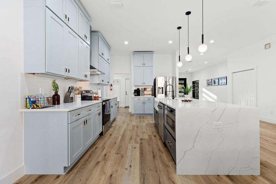 Kitchen featuring light stone counters, stainless steel appliances, pendant lighting, light wood finished floors, and tasteful backsplash