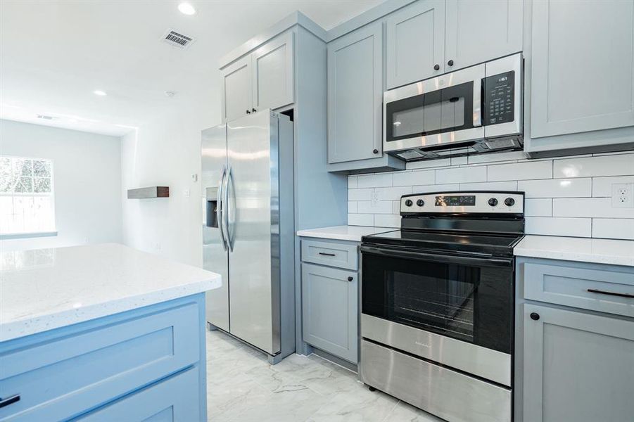 Kitchen featuring light stone counters, stainless steel appliances, light tile patterned floors, and tasteful backsplash