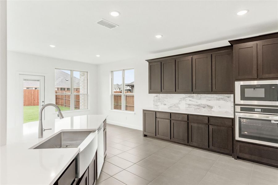 Kitchen with dark wood cabinets, white quartz countertops, farmhouse sink, and stainless steel double oven Kitchen with dark wood cabinets, white quartz countertops, farmhouse sink, and stainless steel double oven