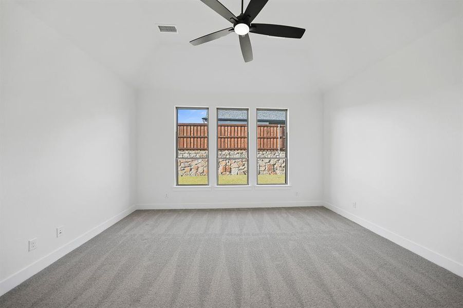 Empty room featuring light carpet, vaulted ceiling, and ceiling fan