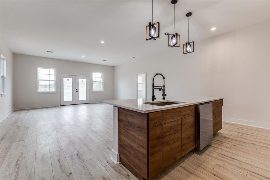 Kitchen with brown cabinetry, light wood-type flooring, a kitchen island with sink, a sink, and open floor plan