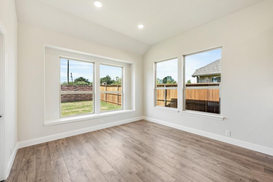 Empty room with light wood floors, white walls, and large windows overlooking a fenced backyard