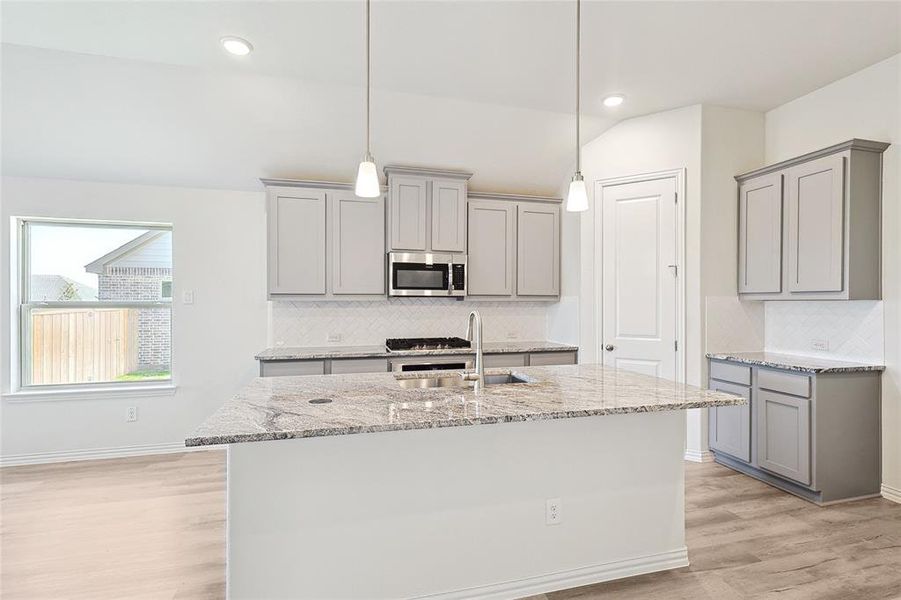 Kitchen with light wood-type flooring, backsplash, gray cabinetry, and sink