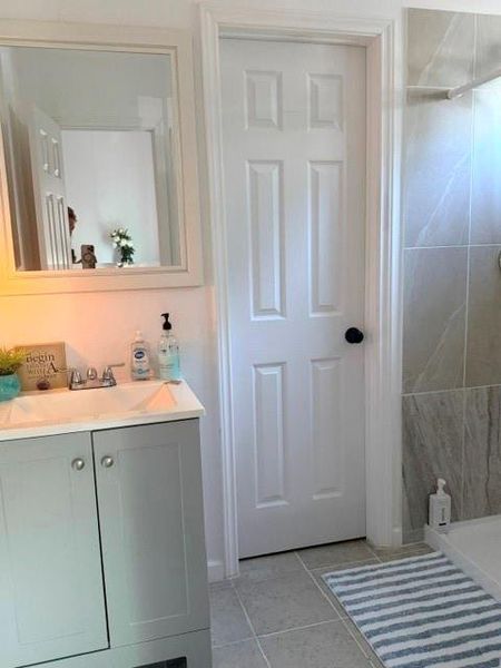 Primary bathroom features a sleek design with a modern vanity, a large mirror, and neutral tile flooring. It includes a walk-in shower with stylish wall tiles and a glass door. The space is well-lit, creating a clean and inviting atmosphere.