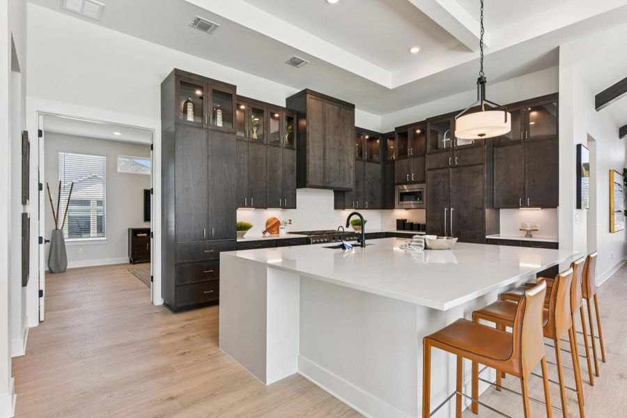 Kitchen with light wood-style flooring, a large island, pendant lighting, glass insert cabinets, and a kitchen breakfast bar