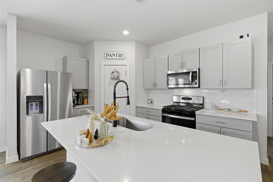 Kitchen with gray cabinetry, stainless steel appliances, a kitchen bar, a center island with sink, and dark wood-type flooring