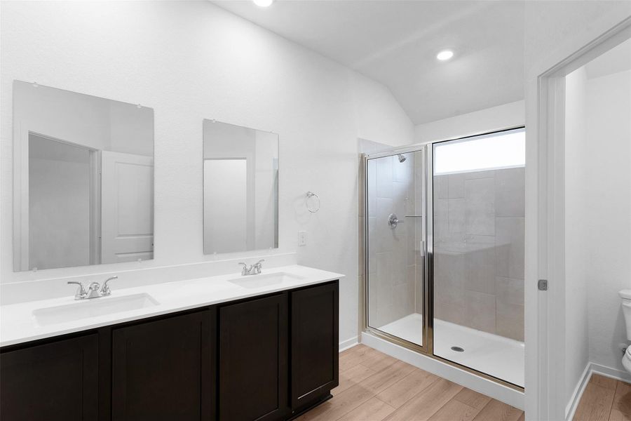 Full bathroom with light wood-style flooring, double vanity, a shower stall, recessed lighting, and vaulted ceiling Full bathroom with light wood-style flooring, double vanity, a shower stall, recessed lighting, and vaulted ceiling