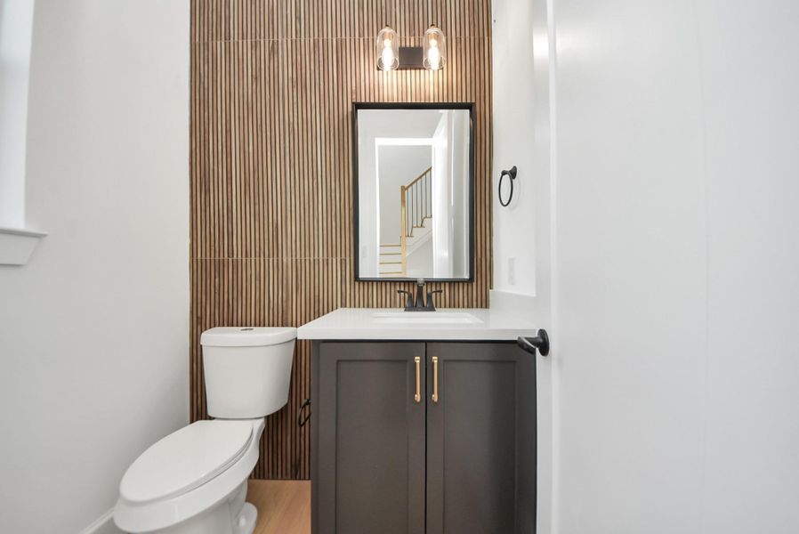 A modern bathroom accented by a warm wood-paneled feature wall, paired with a stylish vanity and gold hardware. Contemporary lighting above the mirror completes the refined look.