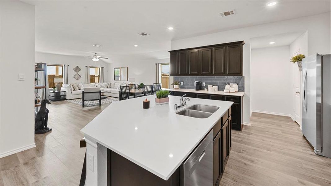 The kitchen features a spacious island with a double sink and a stainless steel dishwasher, dark wood cabinetry, and a grey subway tile backsplash
