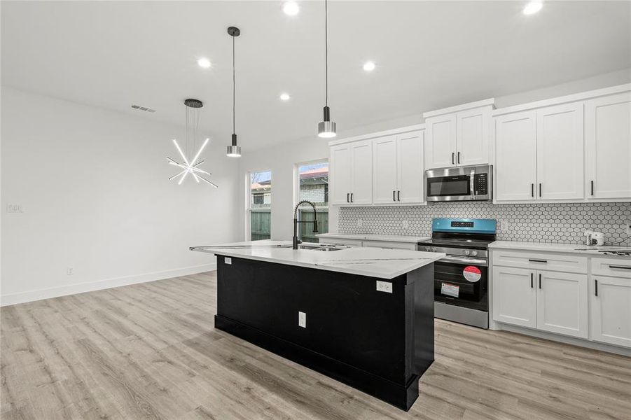 Kitchen featuring white cabinetry, sink, stainless steel appliances, pendant lighting, and a kitchen island with sink