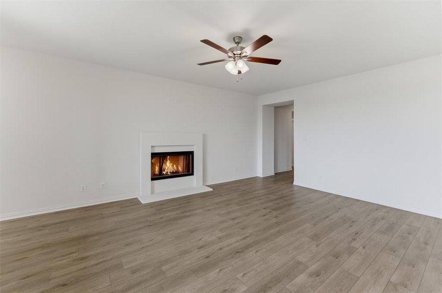 Living space featuring a built-in fireplace with a white mantel, wood-finish flooring, a ceiling fan, and white walls
