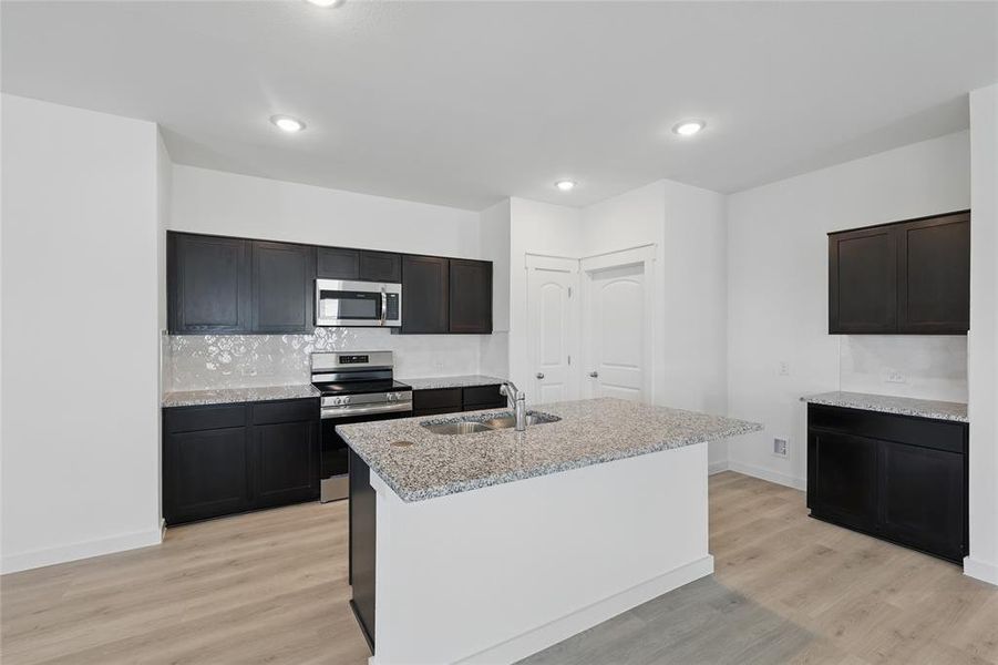 Kitchen with light wood finished floors, a sink, backsplash, and stainless steel appliances Kitchen with light wood finished floors, a sink, backsplash, and stainless steel appliances