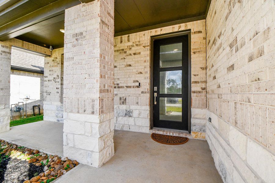 This photo showcases a modern front entrance with a brick exterior and a covered porch area. The black-framed glass door adds a contemporary touch, and the stone pathway enhances the welcoming atmosphere. This photo showcases a modern front entrance with a brick exterior and a covered porch area. The black-framed glass door adds a contemporary touch, and the stone pathway enhances the welcoming atmosphere.