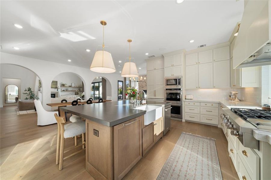 Kitchen featuring sink, hanging light fixtures, stainless steel appliances, premium range hood, and a kitchen island with sink