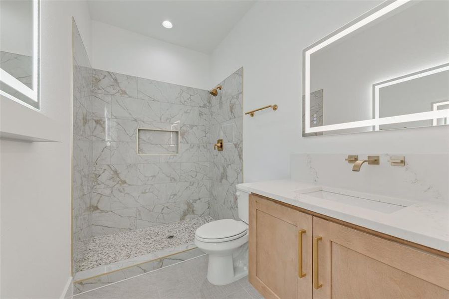 Bathroom with toilet, a tile shower, vanity, and tile patterned floors