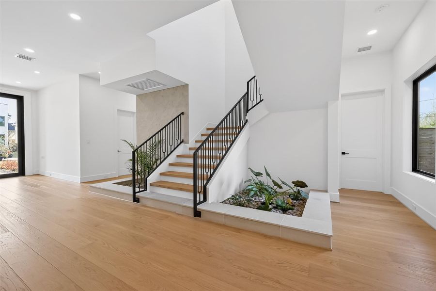 Elegant foyer with iron railing staircase and indoor garden feature.