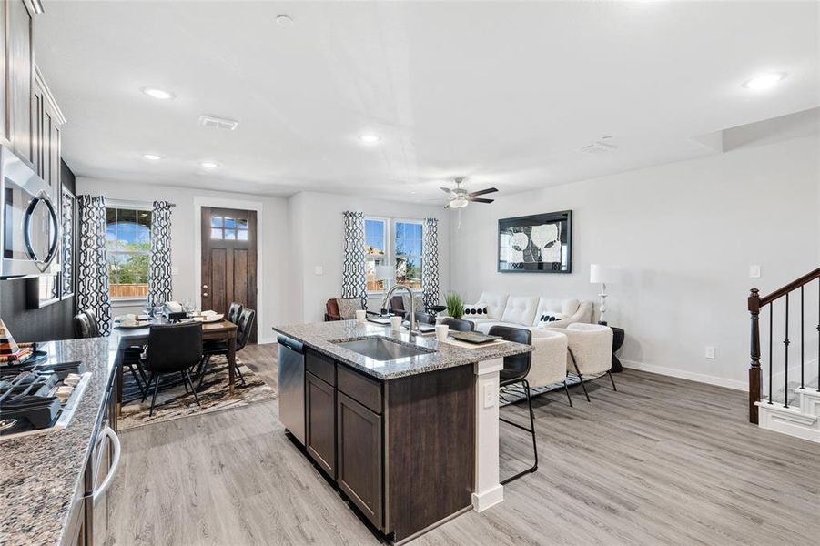 Kitchen featuring light hardwood / wood-style flooring, appliances with stainless steel finishes, sink, ceiling fan, and light stone counters