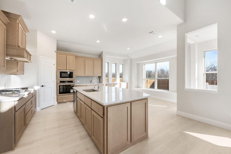 Open kitchen with light wood cabinets, center island with sink, and stainless steel appliances