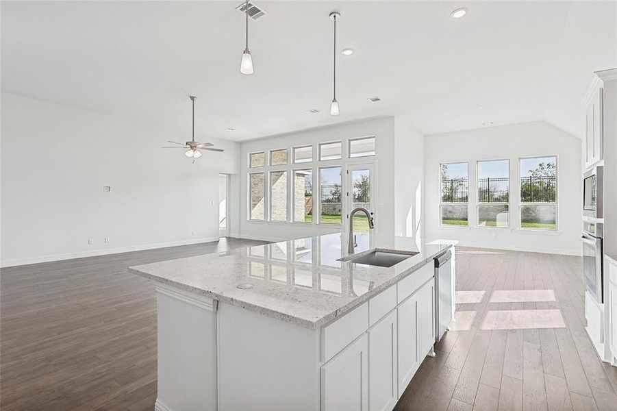 Kitchen with a kitchen island with sink, dark wood-type flooring, stainless steel appliances, sink, and light stone counters