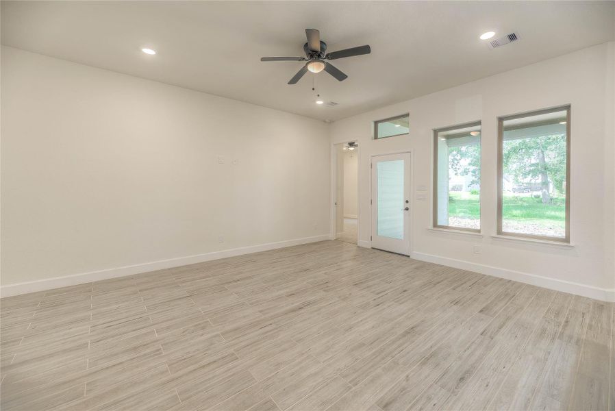 Living Area features light wood-look tile flooring, a ceiling fan, and recessed lighting. Large windows provide ample natural light. The room also includes a modern, frosted glass door, enhancing the contemporary feel.