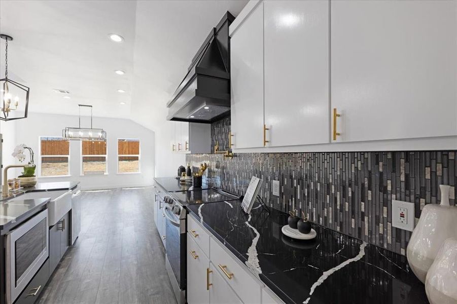 Kitchen with white cabinets, decorative backsplash, custom range hood, appliances with stainless steel finishes, and pendant lighting