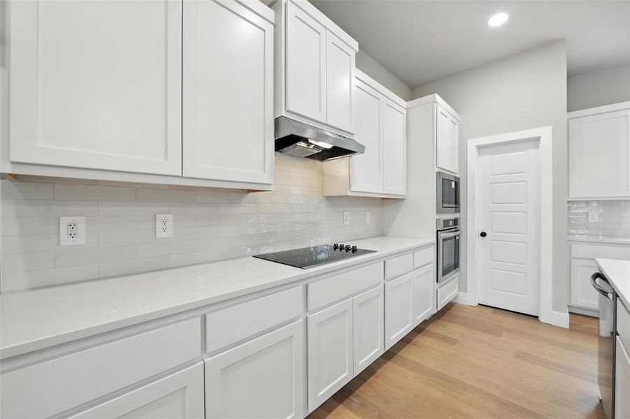 Kitchen with stainless steel appliances, under cabinet range hood, white cabinetry, backsplash, and recessed lighting Kitchen with stainless steel appliances, under cabinet range hood, white cabinetry, backsplash, and recessed lighting