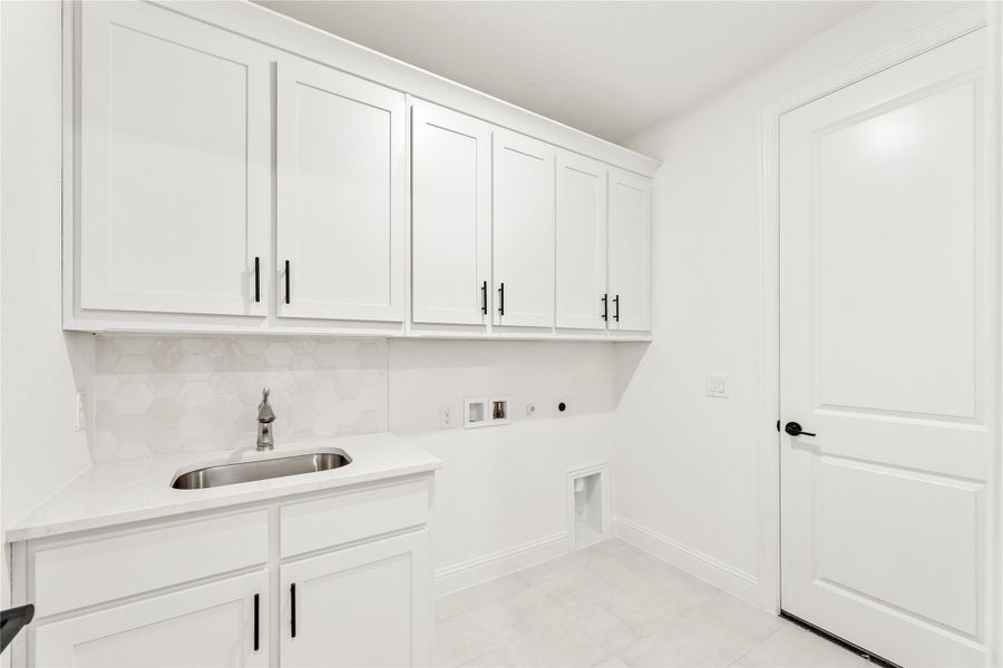 Laundry room with white cabinets, stainless steel sink, hexagon tile backsplash, and washer and dryer hookups.