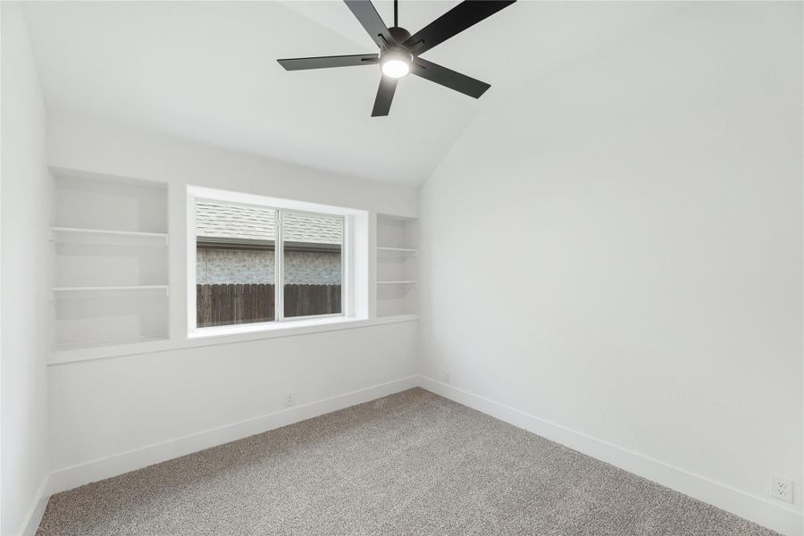 Empty bedroom with vaulted ceiling, black ceiling fan, built-in shelves, and carpet flooring