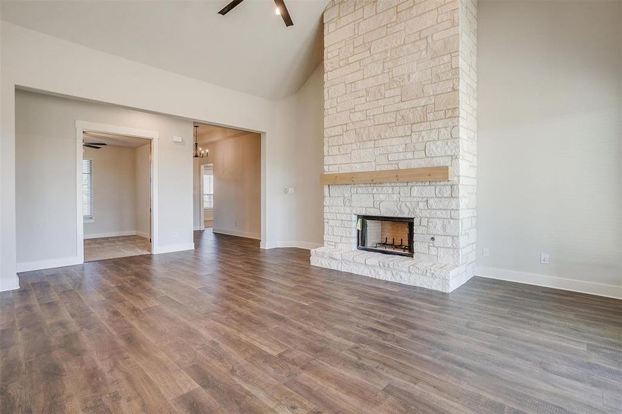 Unfurnished living room featuring high vaulted ceiling, ceiling fan, dark wood-type flooring, and a stone fireplace