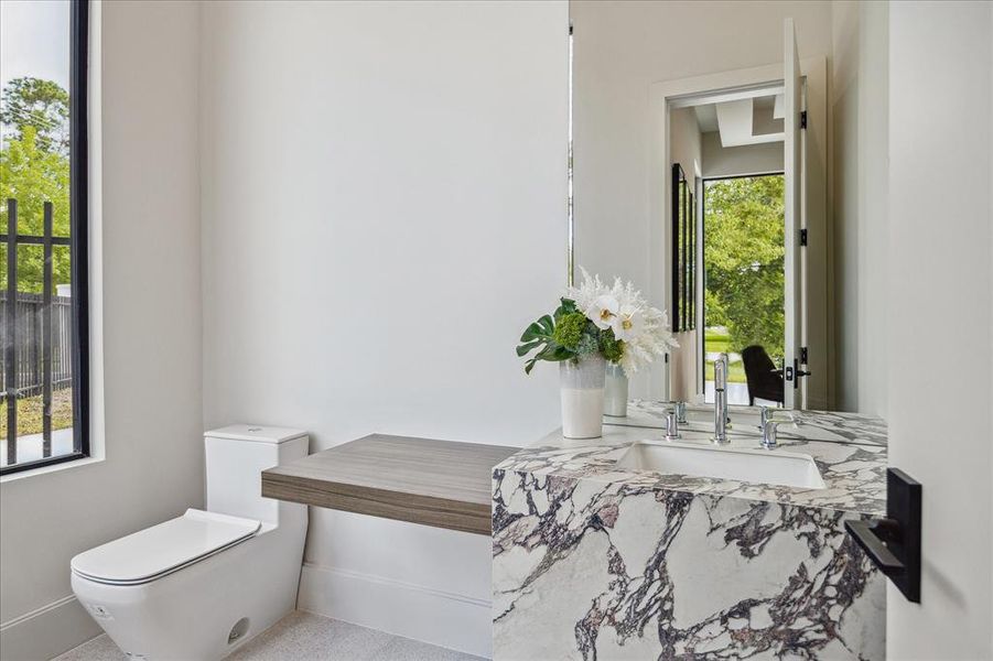 The powder room, conveniently located off the study/office, features porcelain waterfall countertops, Sensei White Lithos floor tile, a Duravit undermount bathroom sink paired with a floating wood shelf and stunning stone countertops. It also includes a Duravit one-piece toilet, combining elegance with functionality in this stylish space.