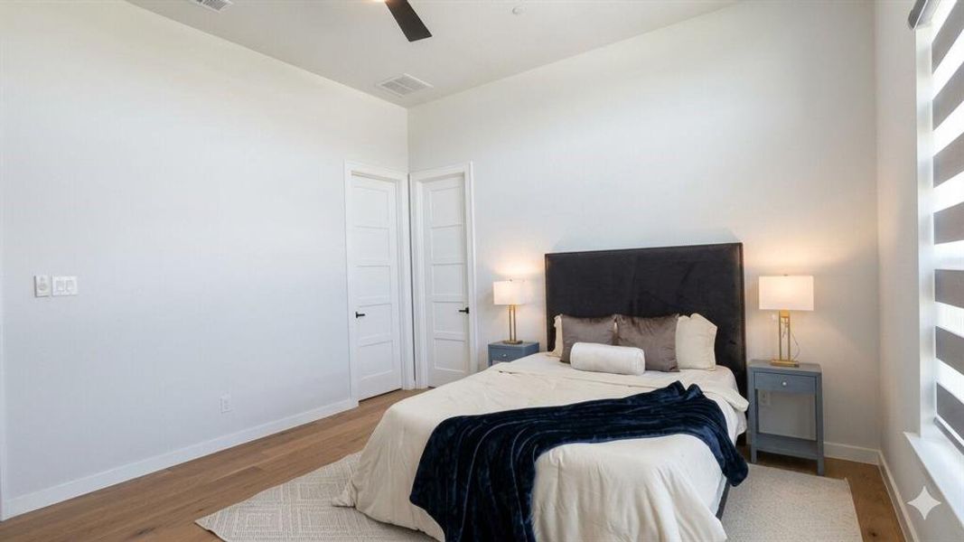 Bedroom featuring wood-finish flooring, two panel-style doors, and a window with horizontal blinds
