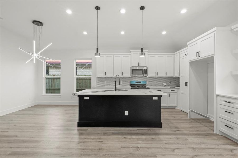 Kitchen with white cabinetry, light hardwood / wood-style flooring, decorative light fixtures, a kitchen island with sink, and appliances with stainless steel finishes