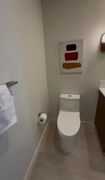 Powder room featuring a dual-flush elongated toilet, wood-finish flooring, wall-mounted brushed nickel towel bar, and a wall-mounted light fixture