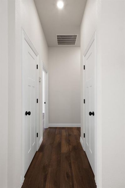 Corridor featuring dark wood-type flooring, visible vents, and baseboards