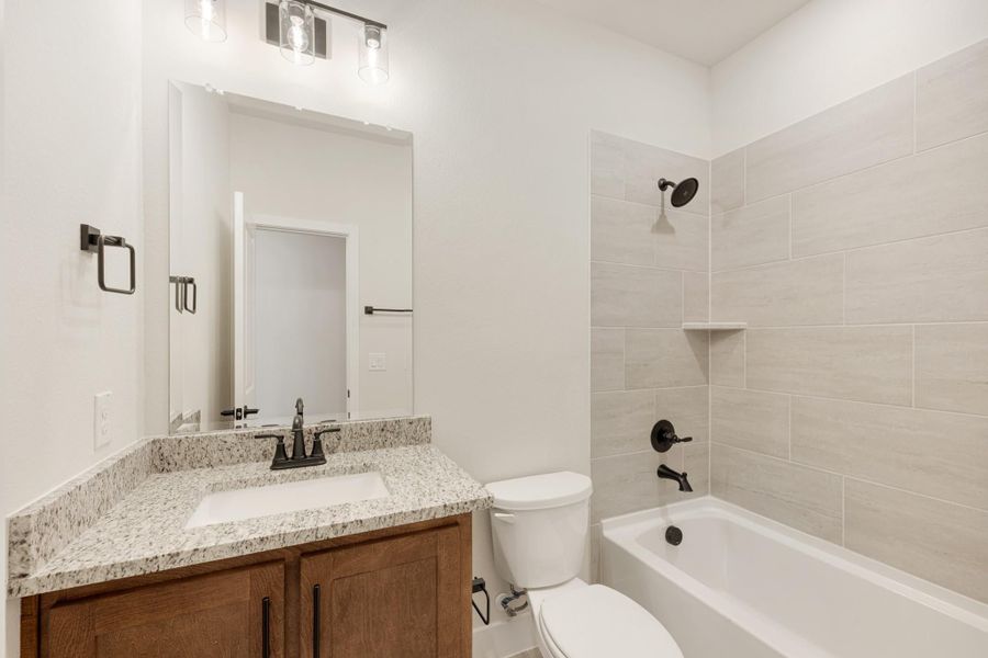 Bathroom with granite vanity, wood cabinets, and tiled tub-shower combo with dark bronze fixtures