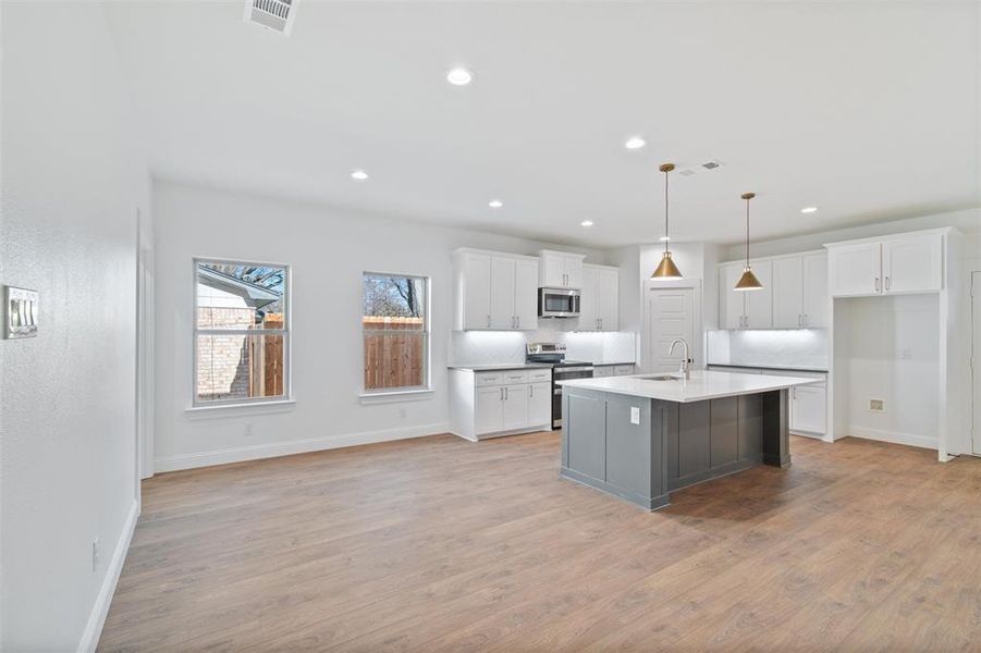 Kitchen featuring backsplash, stainless steel appliances, a kitchen island with sink, pendant lighting, and white cabinetry