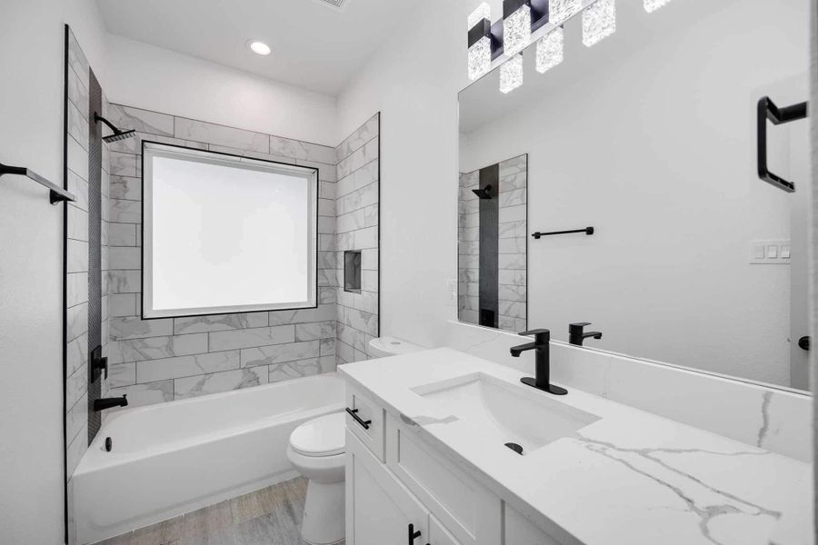 Well-appointed bathroom with quartz vanity, matte black fixtures, tiled shower/tub combination, and a large mirror that enhances the space.